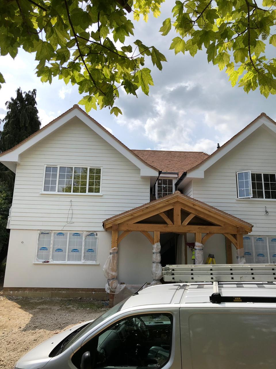 A large home with light exterior finishes and a timber entrance canopy, during construction.